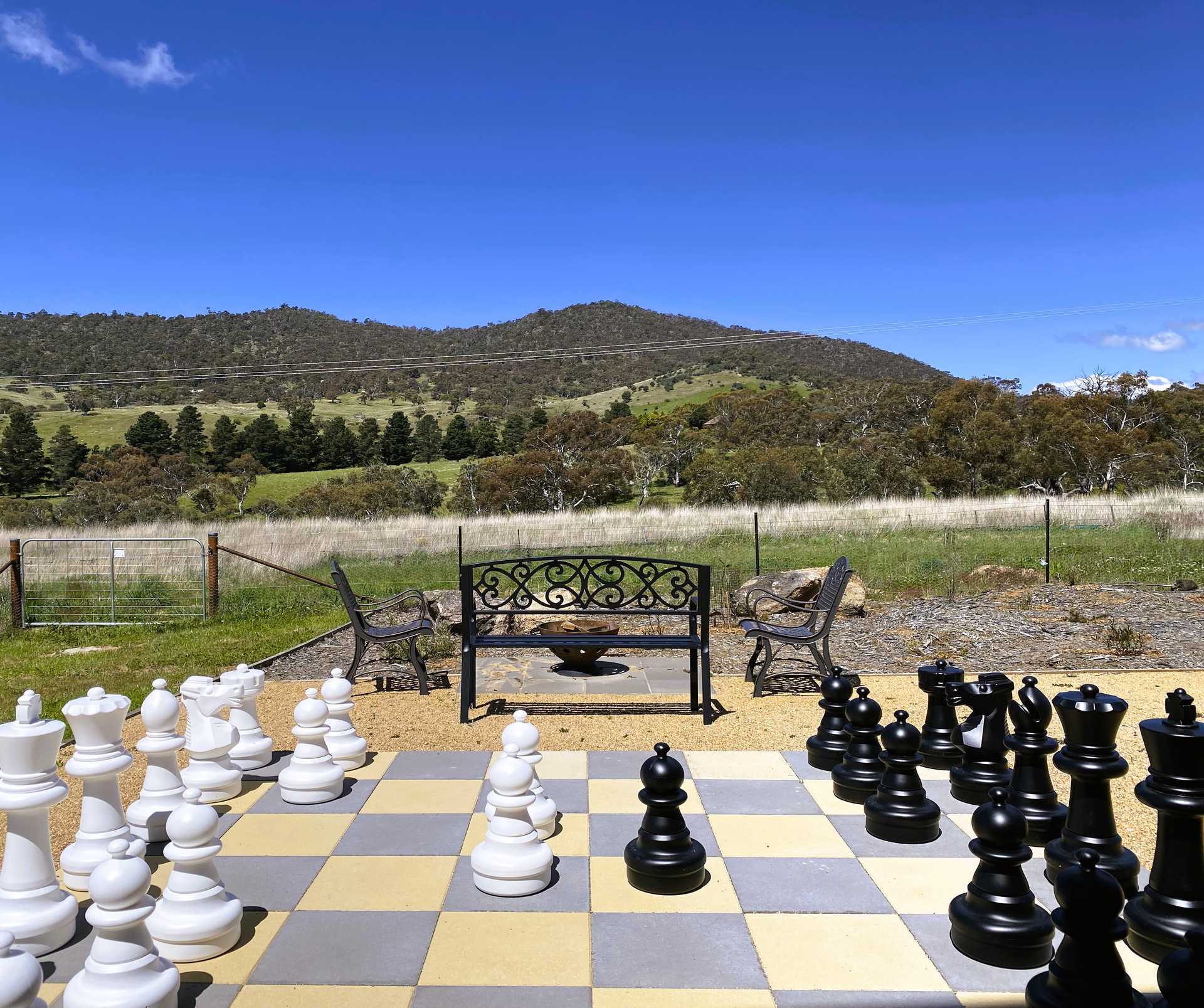 A giant chess set in the foreground, garden bench behind, farmland and hills in the distance